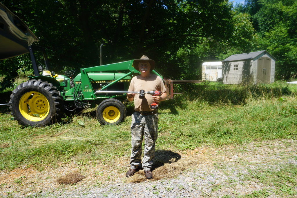 Farmer hold a tool stadning in front of a John Deer tractor