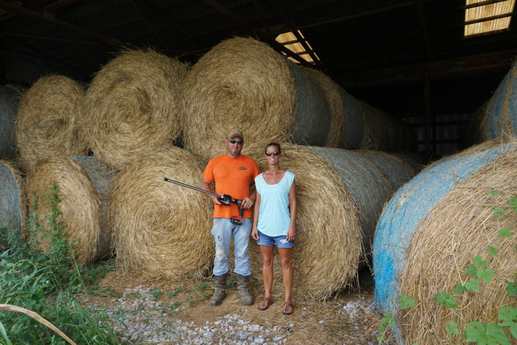 Man and woman standing in front of several bales of hay